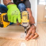 pexels-photo-1249611-1249611 Man using a power drill for home improvement on a wooden floor with precision.